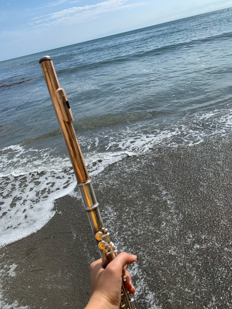 Gold and silver flute held up against ocean waves on the sand
