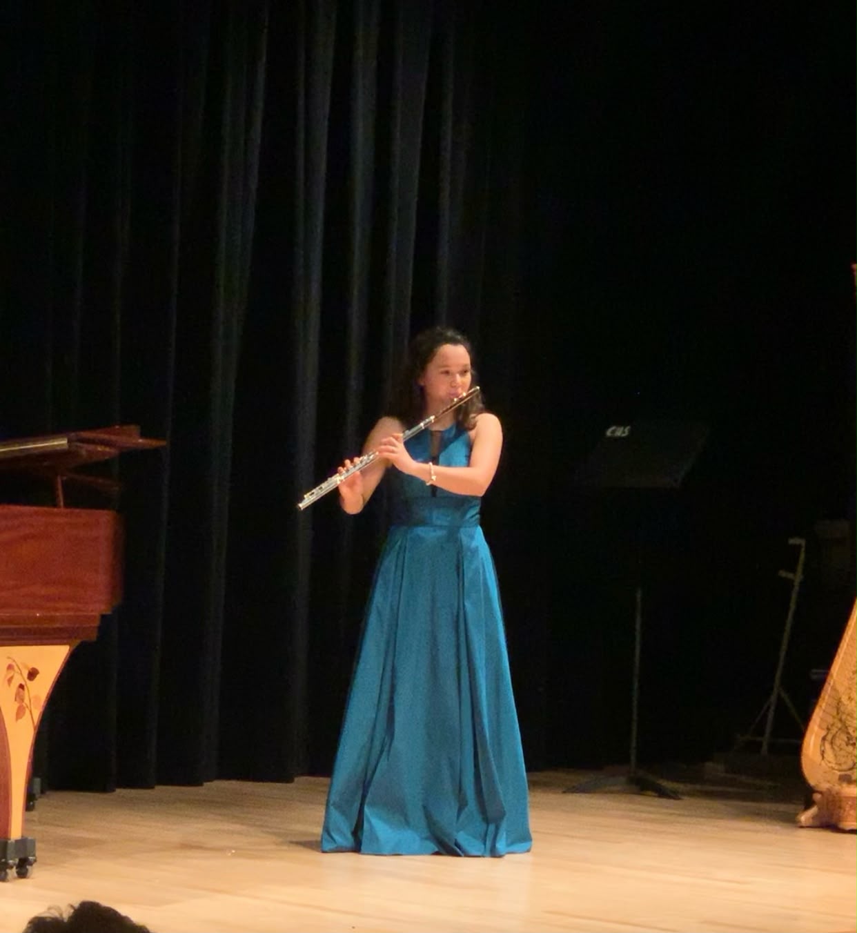 Gabriela Beltrán in a teal gown performing flute solo on a concert hall stage