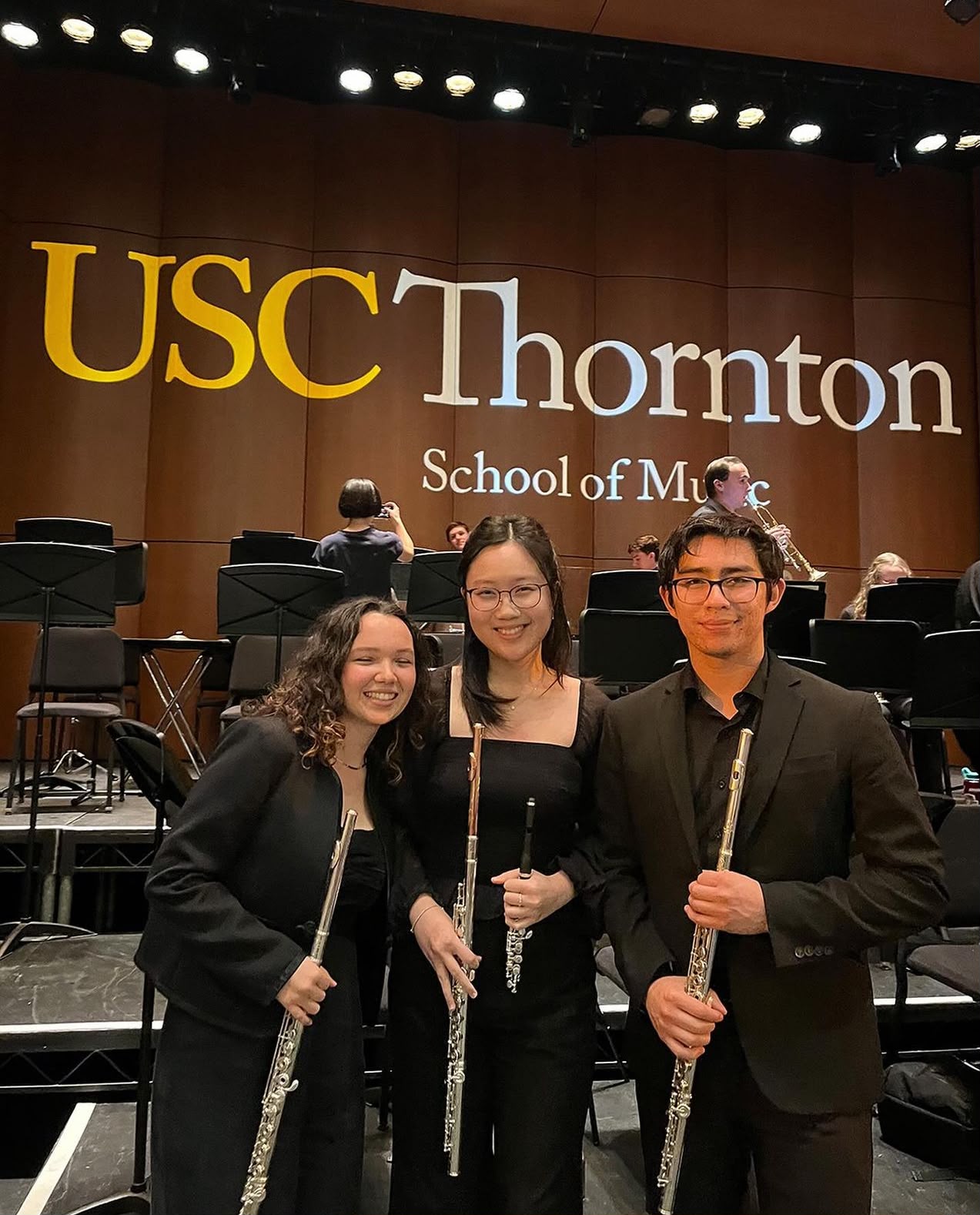 Gabriela Beltrán with two fellow flutists on stage in front of the USC Thornton School of Music backdrop