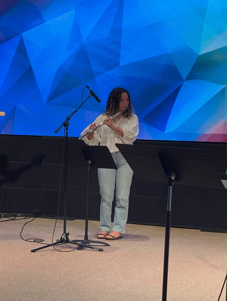 Gabriela Beltrán playing flute at a microphone in front of a blue geometric LED screen