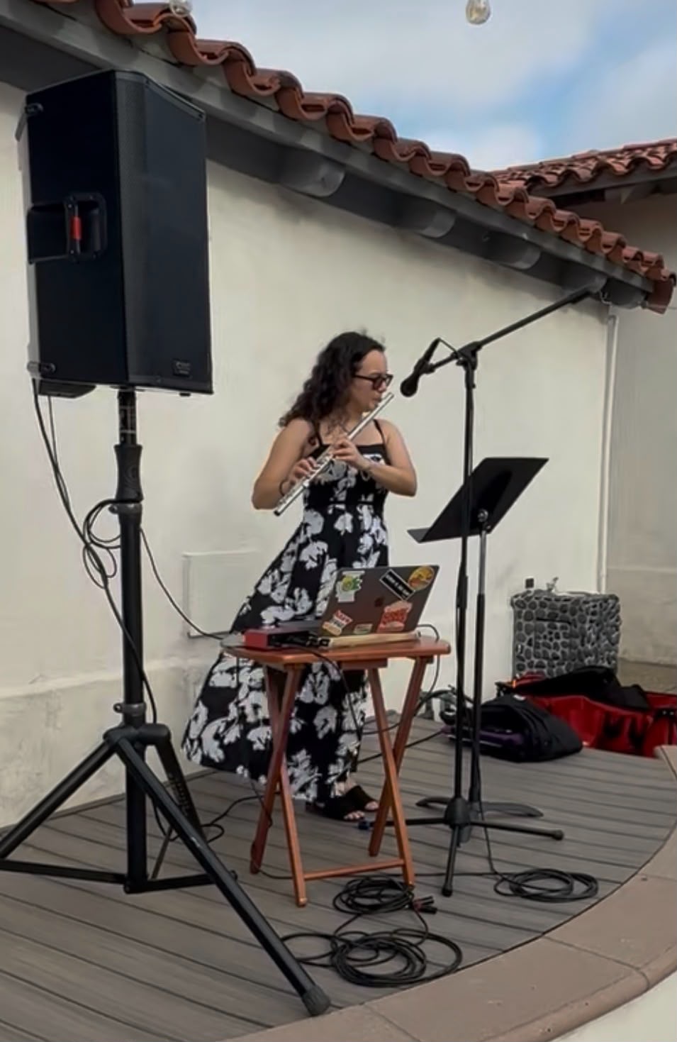 Gabriela Beltrán playing flute with a microphone and speaker at an outdoor patio event