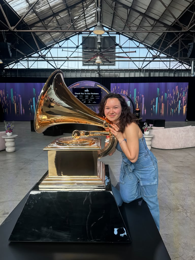 Gabriela Beltrán posing beside a large golden gramophone statue at a Grammy event