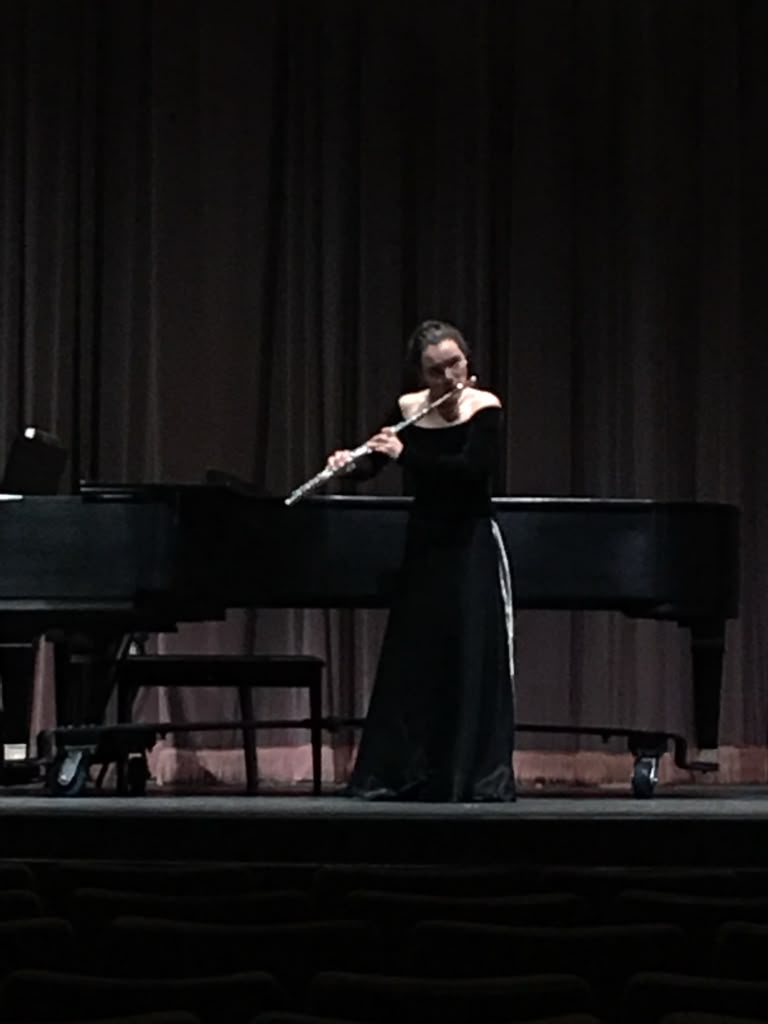 Gabriela Beltrán in a black gown performing flute solo in front of a grand piano