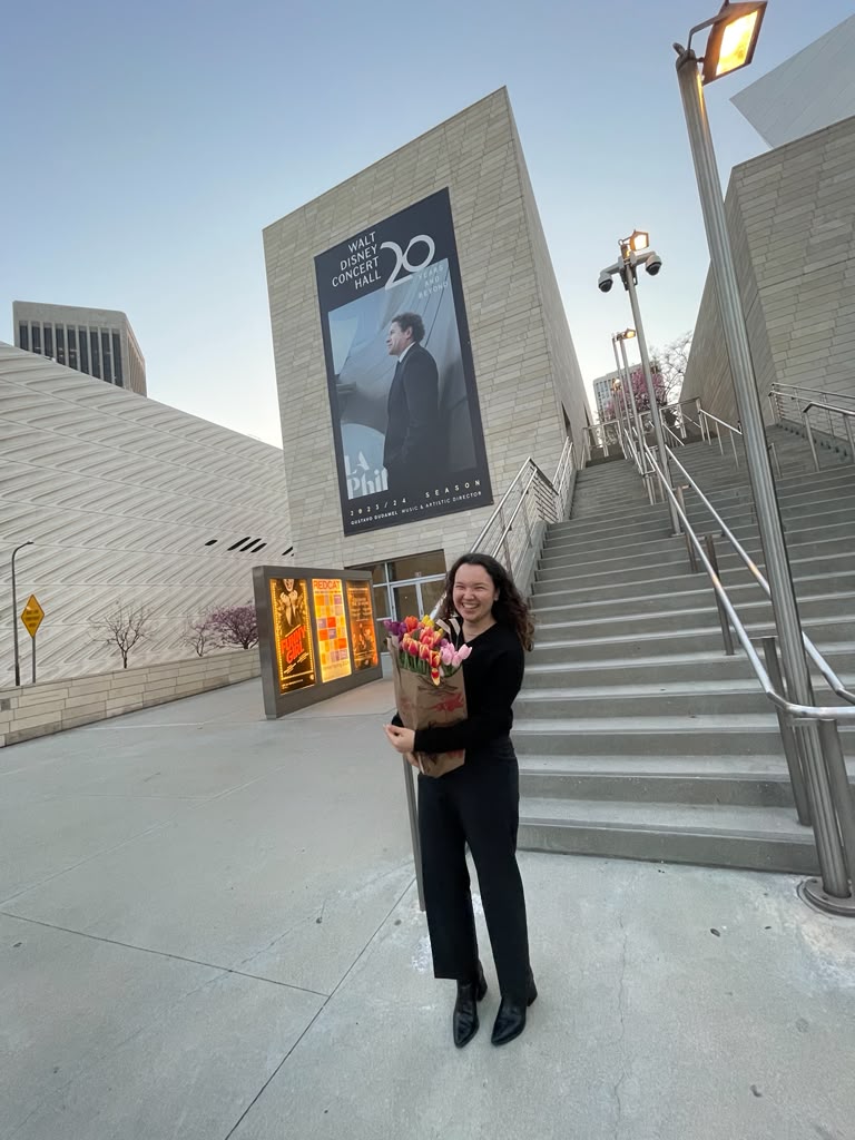 Gabriela Beltrán holding flowers outside Walt Disney Concert Hall at dusk