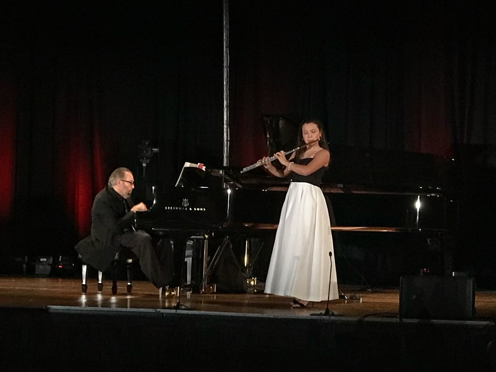 Gabriela Beltrán performing flute with a pianist at a Steinway grand piano on a darkened stage
