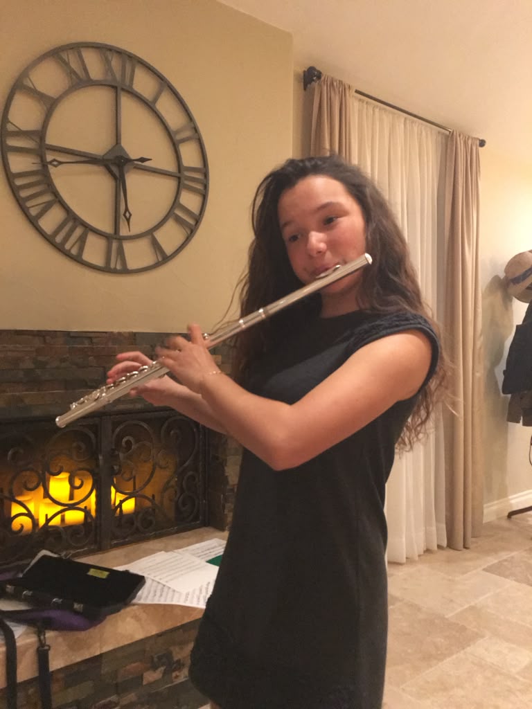 Gabriela Beltrán playing flute at home beside a lit fireplace
