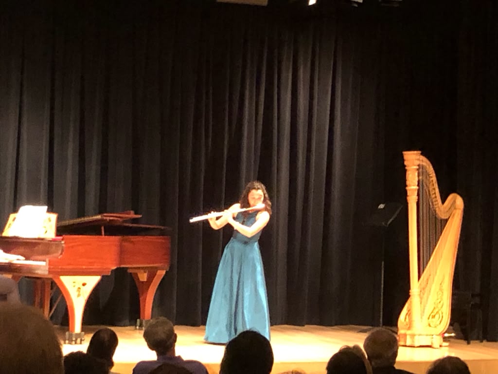 Gabriela Beltrán performing flute on stage beside a grand piano and harp