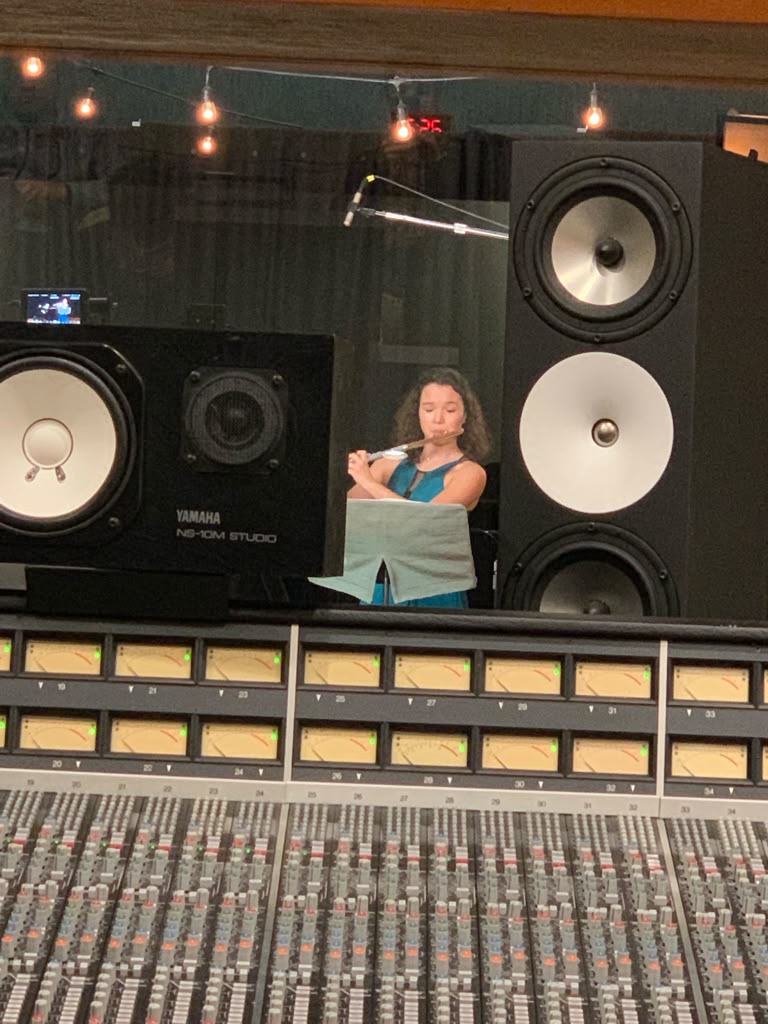 Gabriela Beltrán recording flute seen from behind a large studio mixing console