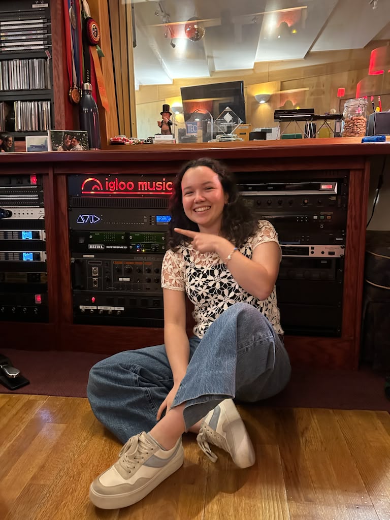 Gabriela Beltrán seated on the floor pointing at the Igloo Music studio sign