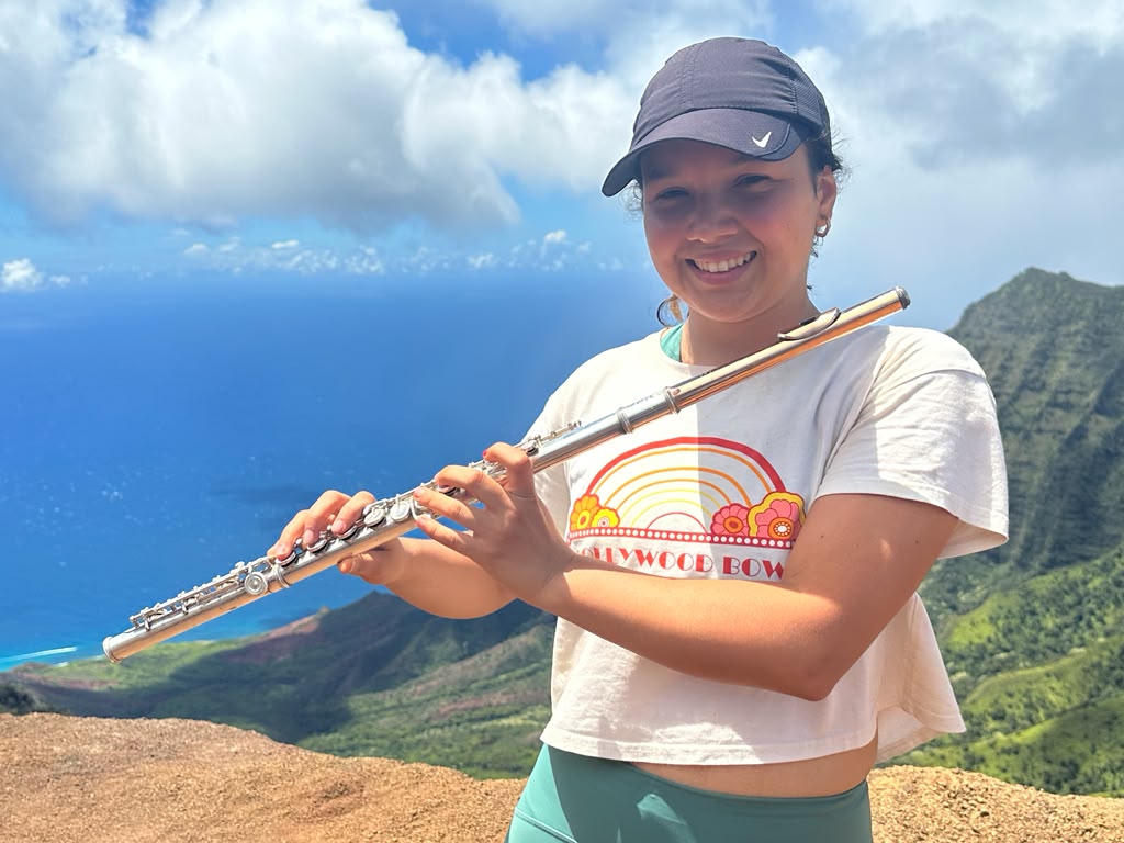 Gabriela Beltrán smiling with her flute on a mountain ridge above the ocean