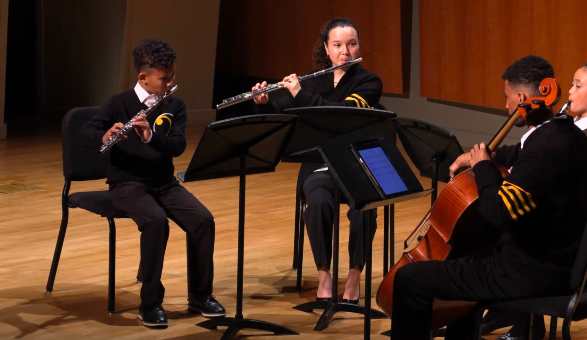 Gabriela Beltrán performing flute in a chamber ensemble with young student musicians on stage