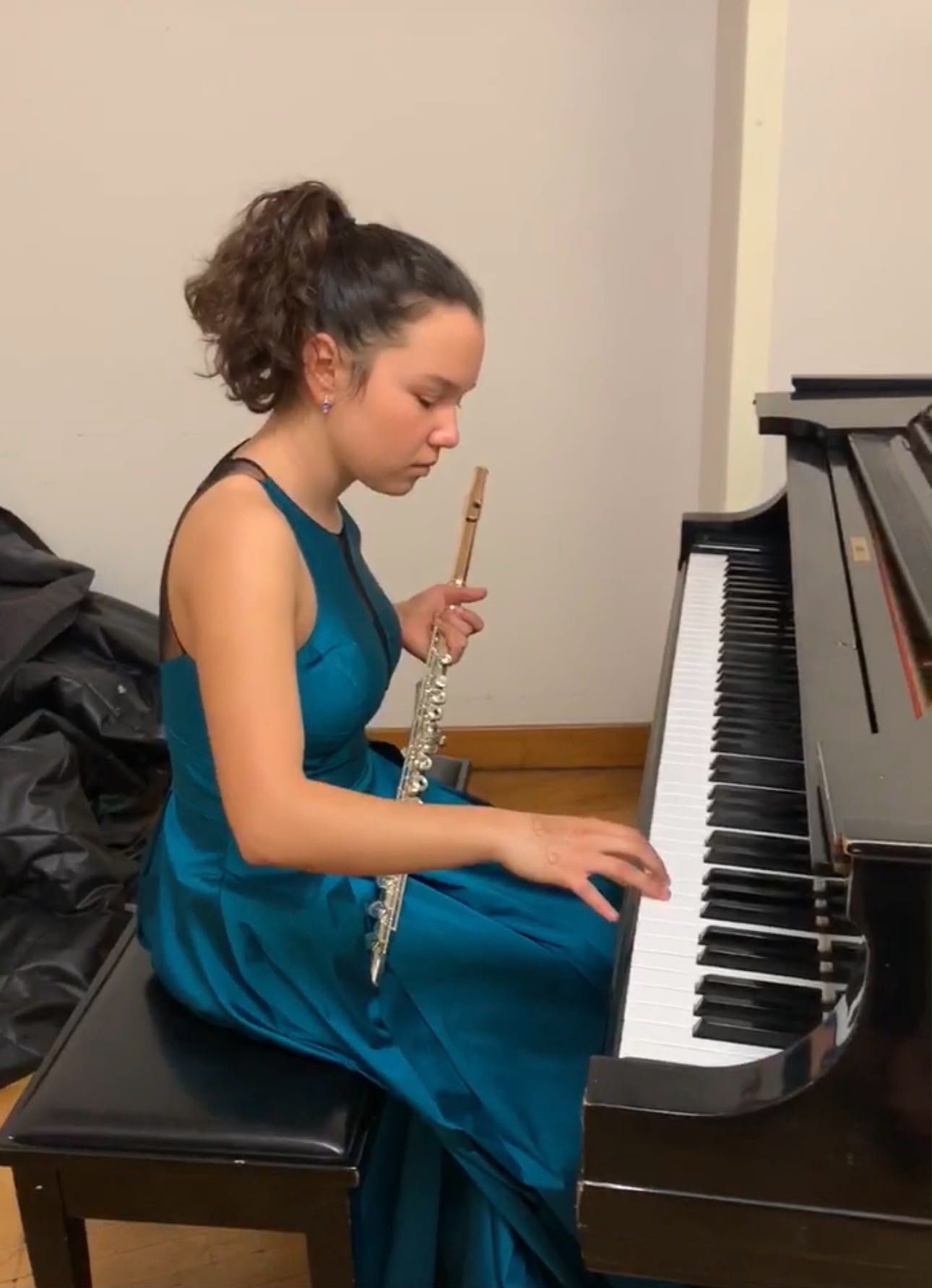 Gabriela Beltrán in a teal gown seated at a grand piano holding her flute