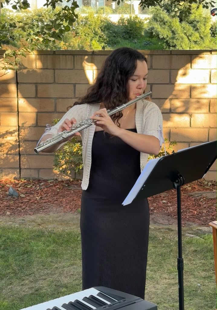 Gabriela Beltrán playing flute outdoors at a garden event beside a keyboard