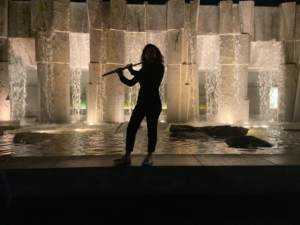 Silhouette of Gabriela Beltrán playing flute in front of an illuminated waterfall wall