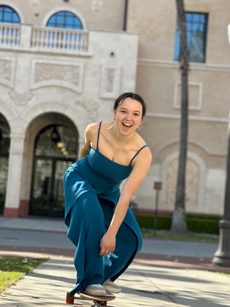 Gabriela Beltrán laughing while riding a skateboard in a teal gown on campus